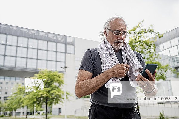 Älterer Mann mit Brille  der ein Smartphone benutzt  während er vor einem klaren Himmel steht