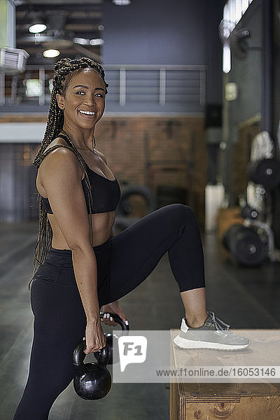 Smiling female athlete lifting kettlebells while standing in gym