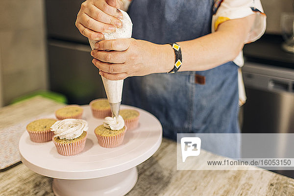 Nahaufnahme einer reifen Frau  die in einer Werkstatt Cupcakes auf einem Tortenständer glasiert