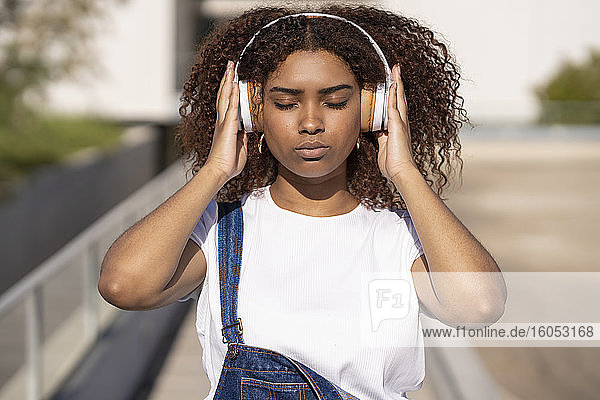 Nahaufnahme einer afroamerikanischen jungen Frau  die in der Stadt stehend Musik über Kopfhörer hört