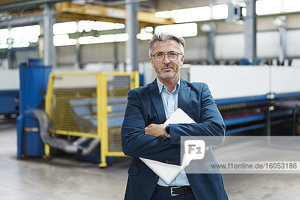 Porträt eines selbstbewussten reifen Geschäftsmannes mit Laptop in einer Fabrik