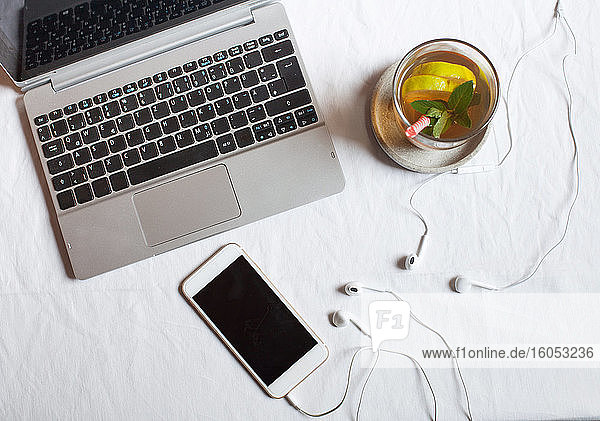 Mobiltelefon mit Kopfhörern und Tee am Laptop auf dem Schreibtisch im Büro