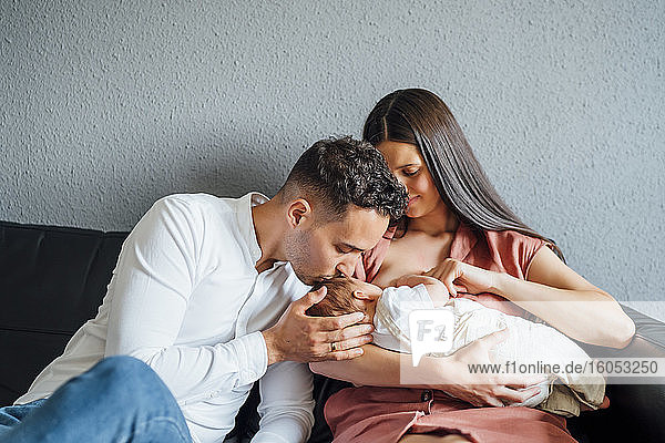 Happy father kissing baby boy being breastfed by mother at home