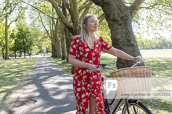 Beautiful woman walking with bicycle on footpath in public park