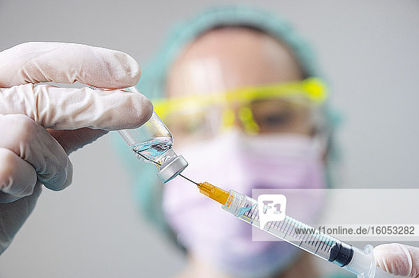 Nahaufnahme der Hände eines Zahnarztes  der den Coronavirus-Impfstoff und die Spritze in der Klinik hält