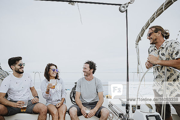 Fröhliche Freunde haben Spaß und genießen Bier auf einem Segelboot gegen den klaren Himmel