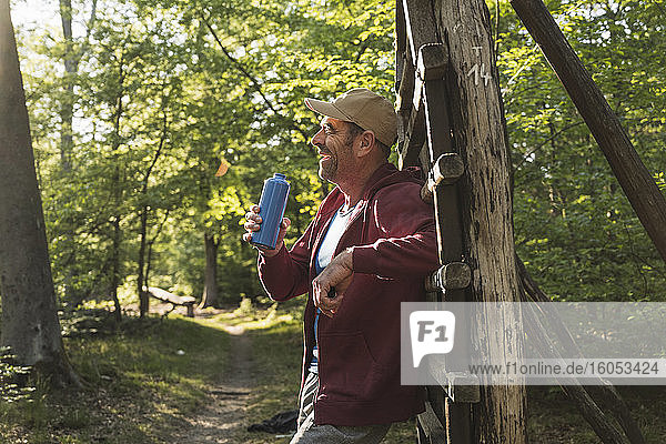 Lächelnder reifer Mann  der eine Wasserflasche hält  während er an einer Holzleiter im Park steht