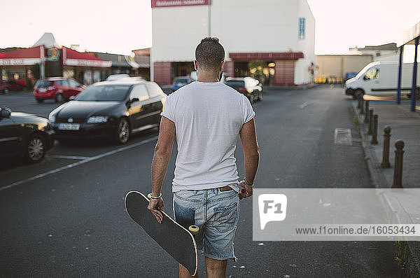 Junger Mann mit Skateboard auf der Straße in der Stadt