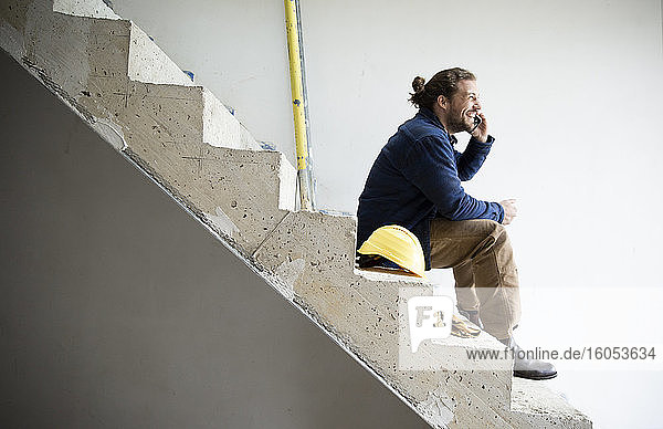 Bauarbeiter  der über sein Smartphone spricht  während er auf einer Treppe sitzt  um ein Haus zu bauen
