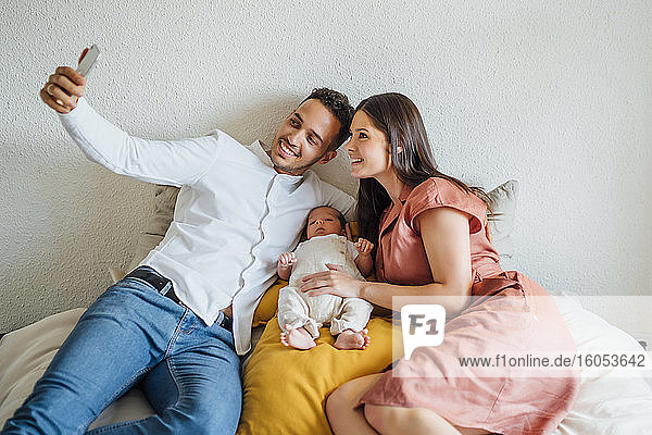 Glückliche Eltern nehmen Selfie mit Baby Junge im Schlafzimmer zu Hause