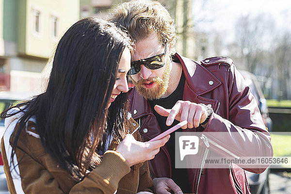 Nahaufnahme eines jungen Paares  das ein Smartphone benutzt  während es an einem sonnigen Tag im Freien sitzt