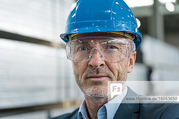 Porträt eines reifen Geschäftsmannes mit Schutzhelm und Schutzbrille in einer Fabrik