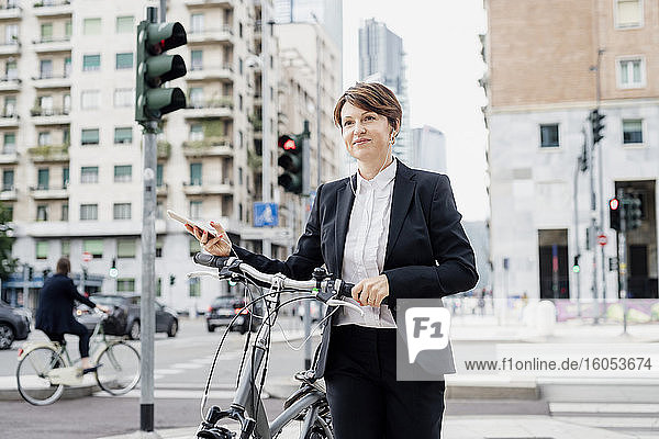 Female professional listening music while walking with bicycle on street in city