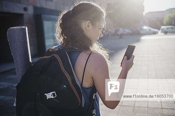 Sportliche junge Frau  die ihr Smartphone benutzt  während sie an einem sonnigen Tag durch die Stadt läuft