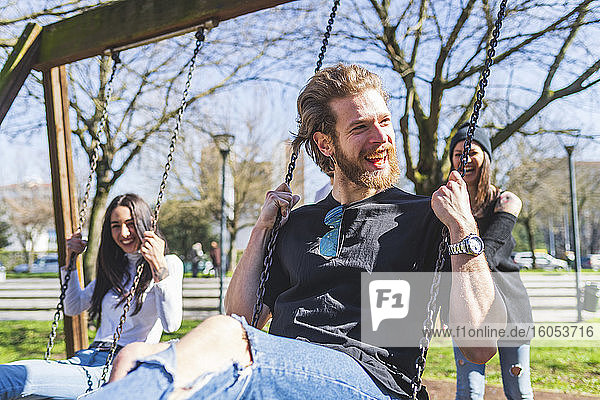 Cheerful friends swinging in park during sunny day