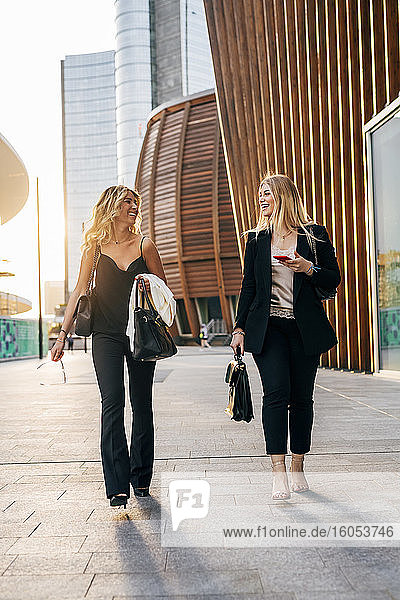 Female colleagues talking while walking on sidewalk in city