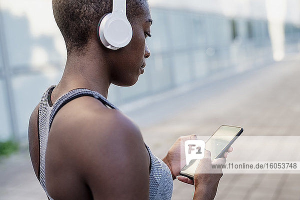 Nahaufnahme einer jungen Frau mit Kopfhörern  die ein Smartphone benutzt  während sie in der Stadt steht