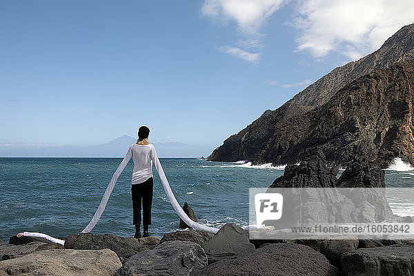 Frau mit künstlichen langen Händen steht auf Felsen am Strand gegen den Himmel