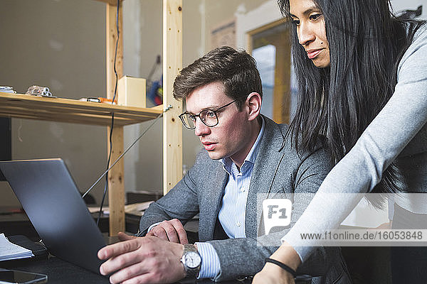 Geschäftsmann und Frau teilen sich einen Laptop am Schreibtisch im Büro
