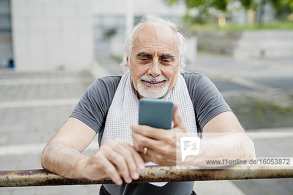 Nahaufnahme eines älteren Mannes  der sein Smartphone benutzt  während er an einem Geländer steht