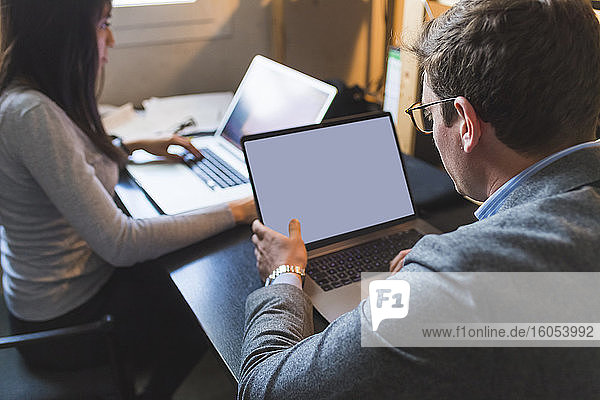 Businessman and woman using laptops at desk in office
