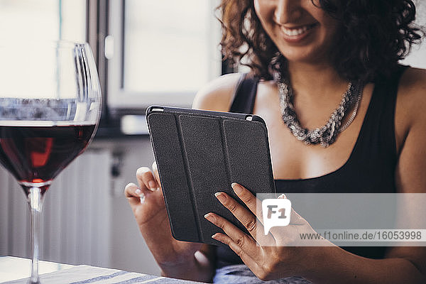 Lächelnde junge Frau  die ein digitales Tablet benutzt  während sie am Esstisch sitzt
