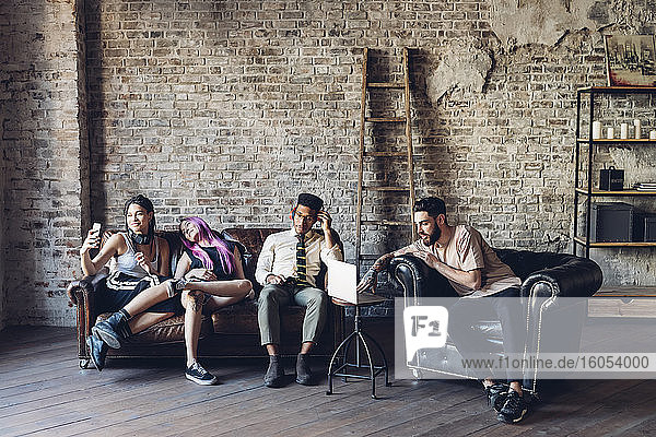 Eine Gruppe von Freunden sitzt auf einem Sofa in einem Loft und nutzt Technologie
