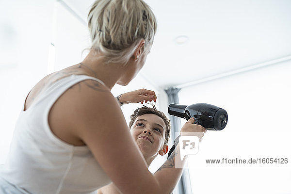 Female hairdresser drying boy's hair at home