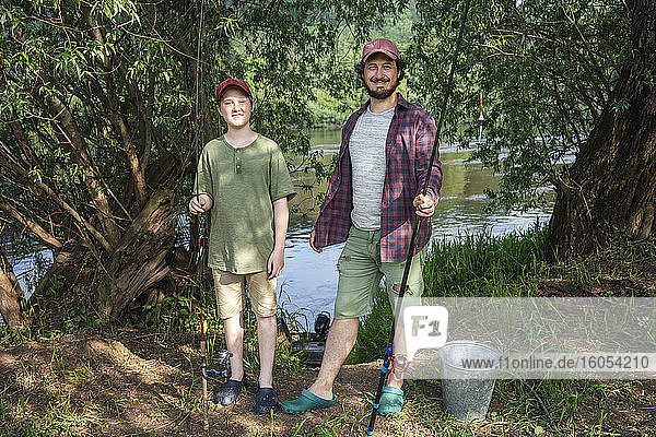 Vater und Sohn halten Angelruten am Flussufer