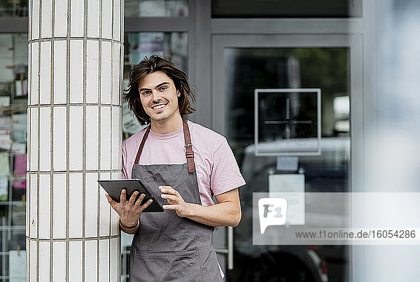 Lächelnder Besitzer  der ein digitales Tablet benutzt  während er an einer Säule vor einem Café steht