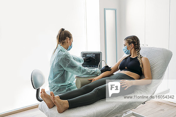 Arzt mit Gesichtsmaske bei der Untersuchung einer Sportlerin mit einem Ultraschallgerät
