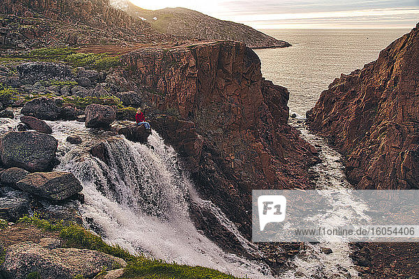 Junge Frau sitzt auf einem Felsen am Wasserfall  Teriberka  Murmansk Oblast  Russland