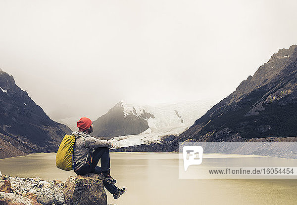 Mann mit Rucksack sitzt auf einem Felsen am See in Patagonien  Argentinien