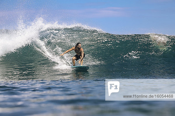 Männlicher Surfer ohne Hemd  der auf dem Meer gegen den Himmel surft  Bali  Indonesien