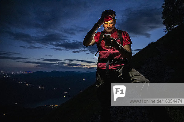 Männlicher Wanderer  der nachts auf einem Berg steht und über sein Smartphone die Karte überprüft  Orobie  Lecco  Italien