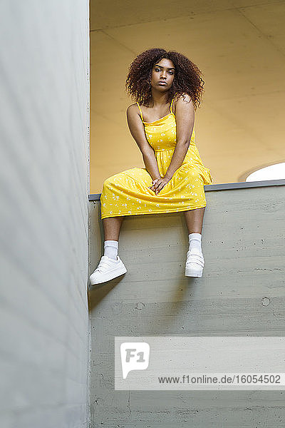 Junge afroamerikanische Frau in gelbem Kleid sitzt auf einer Stützmauer