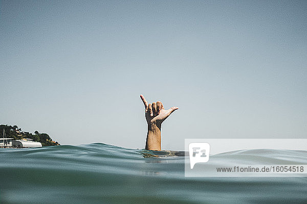 Frauenhand macht Surfer-Zeichen im Wasser