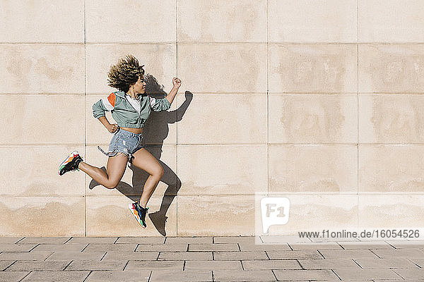 Young woman jumping against wall during sunny day