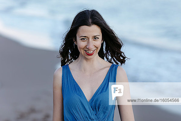 Dunkelhaarige Frau in blauem Kleid am Strand  lächelnd  Porträt