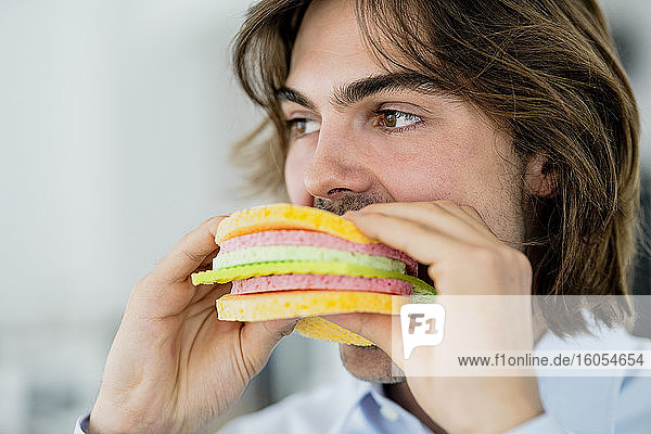 Nahaufnahme eines Geschäftsmannes  der wegschaut  während er in einem Café einen Schwammtuch-Burger isst
