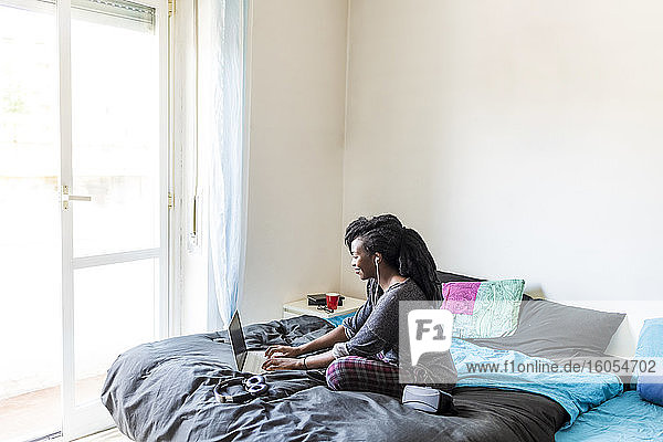 Junge Frau mit Laptop auf dem Bett zu Hause