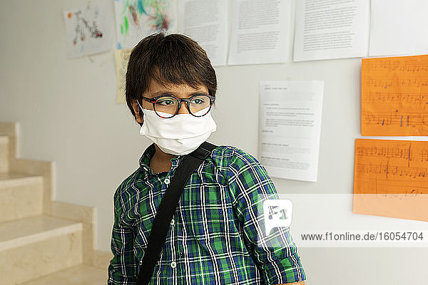 Junge mit Maske  der wegschaut  während er in der Schule an der Wand steht