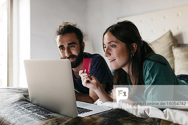 Happy couple lying on bed shopping online