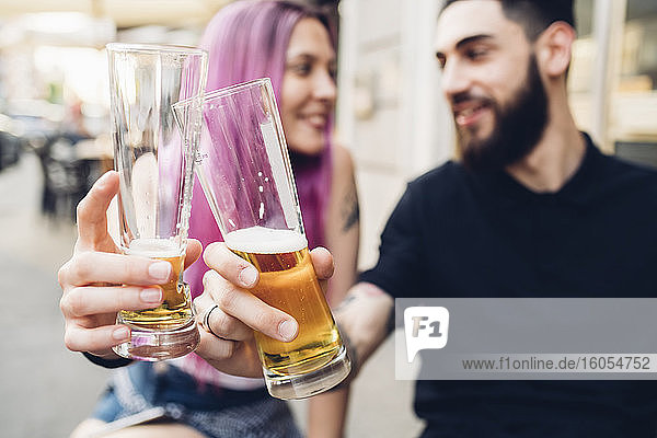 Glückliches junges Paar stößt im Freien an einer Bar mit Biergläsern an