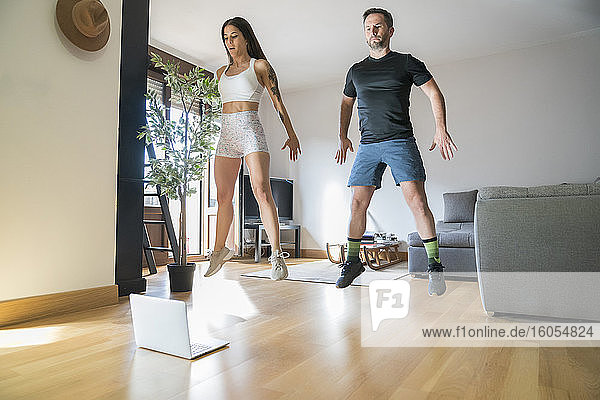Couple jumping while exercising on hardwood floor at home
