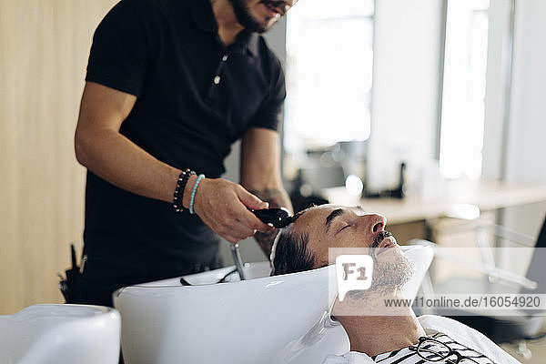 Friseurin wäscht die Haare eines Kunden im Friseursalon