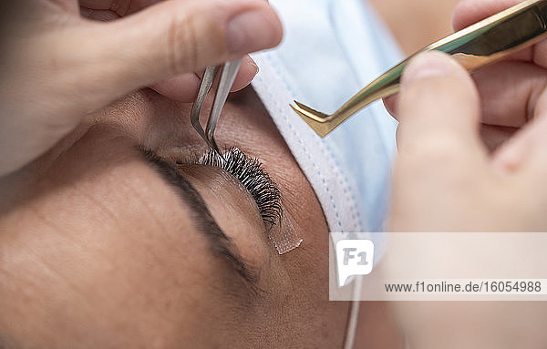 Close-up of beautician using tweezers on customer for eyelash extension at beauty spa