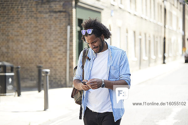 Young man with backpack standing on street looking at cell phone  London  UK