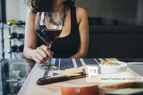 Junge Frau hält ein Weinglas  während sie am Esstisch sitzt