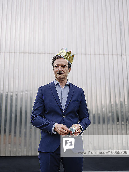 Portrait of a mature businessman wearing a toy crown holding protective face mask